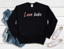 Load image into Gallery viewer, Softest Crewneck Sweatshirt. Designed to elevate your vibe to help you live your intention. We see you strive to surround yourself in love.     You can consciously create your internal state when you practice living with love. Choosing peace, joy, compassion, gratitude and mindfulness,  over and over and over, babe. Practice living with love, babe. For yourself and others, and radiate the loving human that you are. Black crewneck sweatshirt with white love babe print and pink lips for the o in love.
